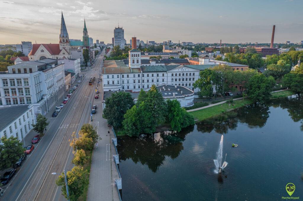 Zdjęcie z drona przedstawiające klasycystyczny, biały kompleks fabryczny Ludwika Geyera z lotu ptaka, otoczony zielenią i stawem.