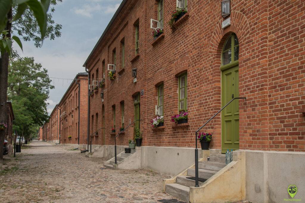 Długa, klimatyczna aleiczka biegnąca wzdłuż jednolitych, czerwonych budynków z cegły (famułów) na osiedlu Księży Młyn Łódź.