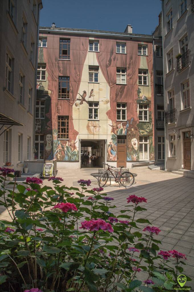 Podwórko Narodzin Dnia przy Piotrkowskiej z kolorowymi, surrealistycznymi instalacjami na ścianach.
